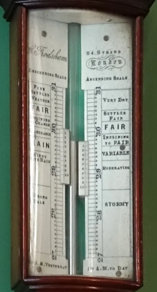 The dial of a Victorian mercury stick barometer: two vertical scales in inches from 27 to 31 either side of the glass tube, with weather words beside them from Very Dry and Fair at the top to Rain, Strong Gale and Stormy at the bottom, and a sliding pointer on each scale.