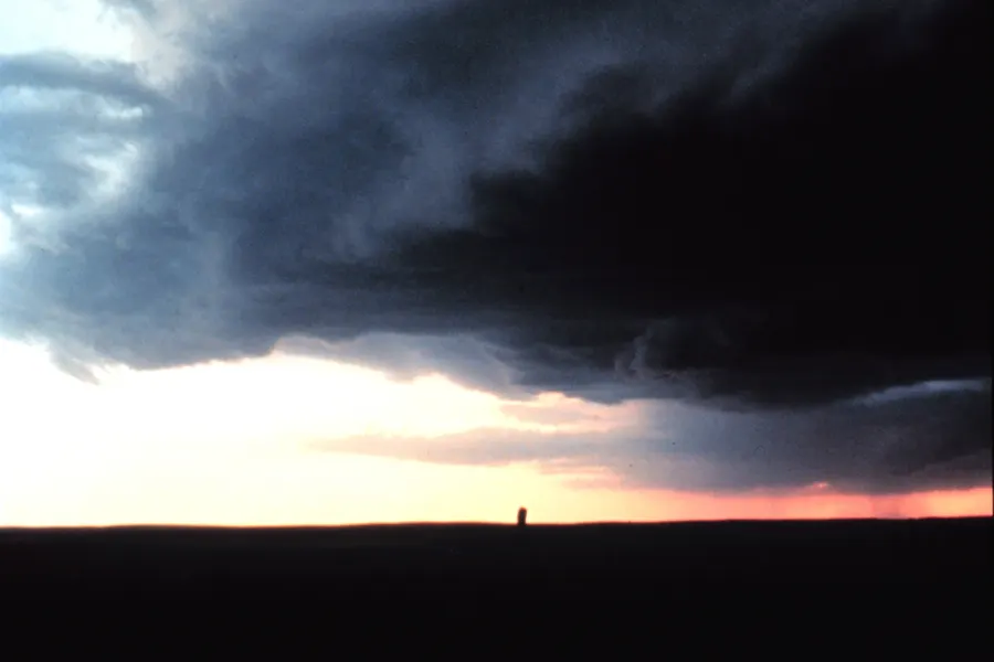 The dark, layered leading edge of a storm cloud overhanging a flat horizon, with bright evening sky beneath it.