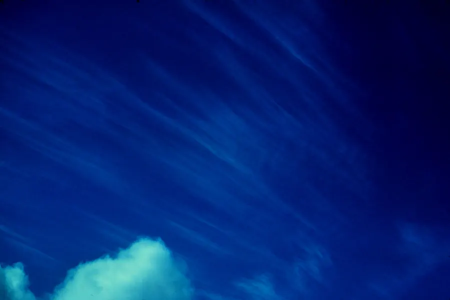 Long white streaks and wisps of thin cloud slanting across a deep blue sky, with the top of a small white cumulus in the lower corner.