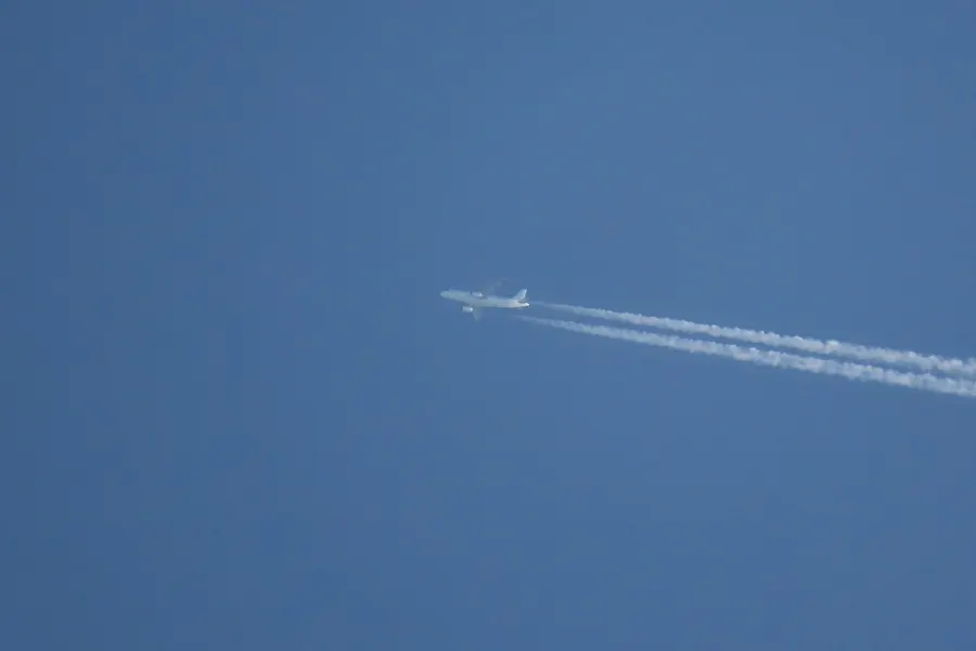 An airliner high in a clear blue sky trailing two long white condensation trails.
