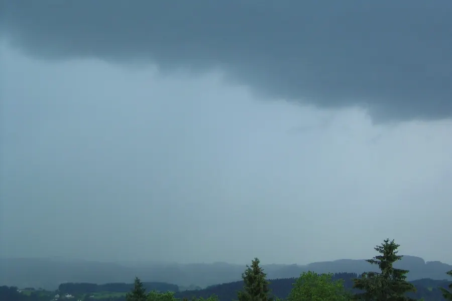 A dark gray cloud base overhead, with a veil of rain hiding the hills and forest in the distance.
