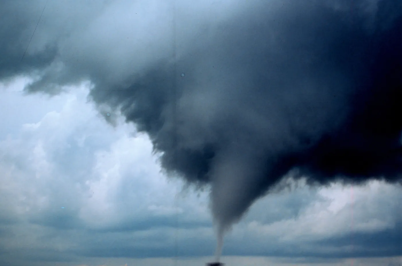 A smooth cone-shaped tornado descends from a ragged, rotating cloud base filling the frame.