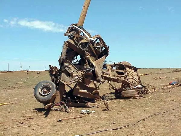 A pickup truck wrapped around a utility pole with most of its bodywork stripped away.