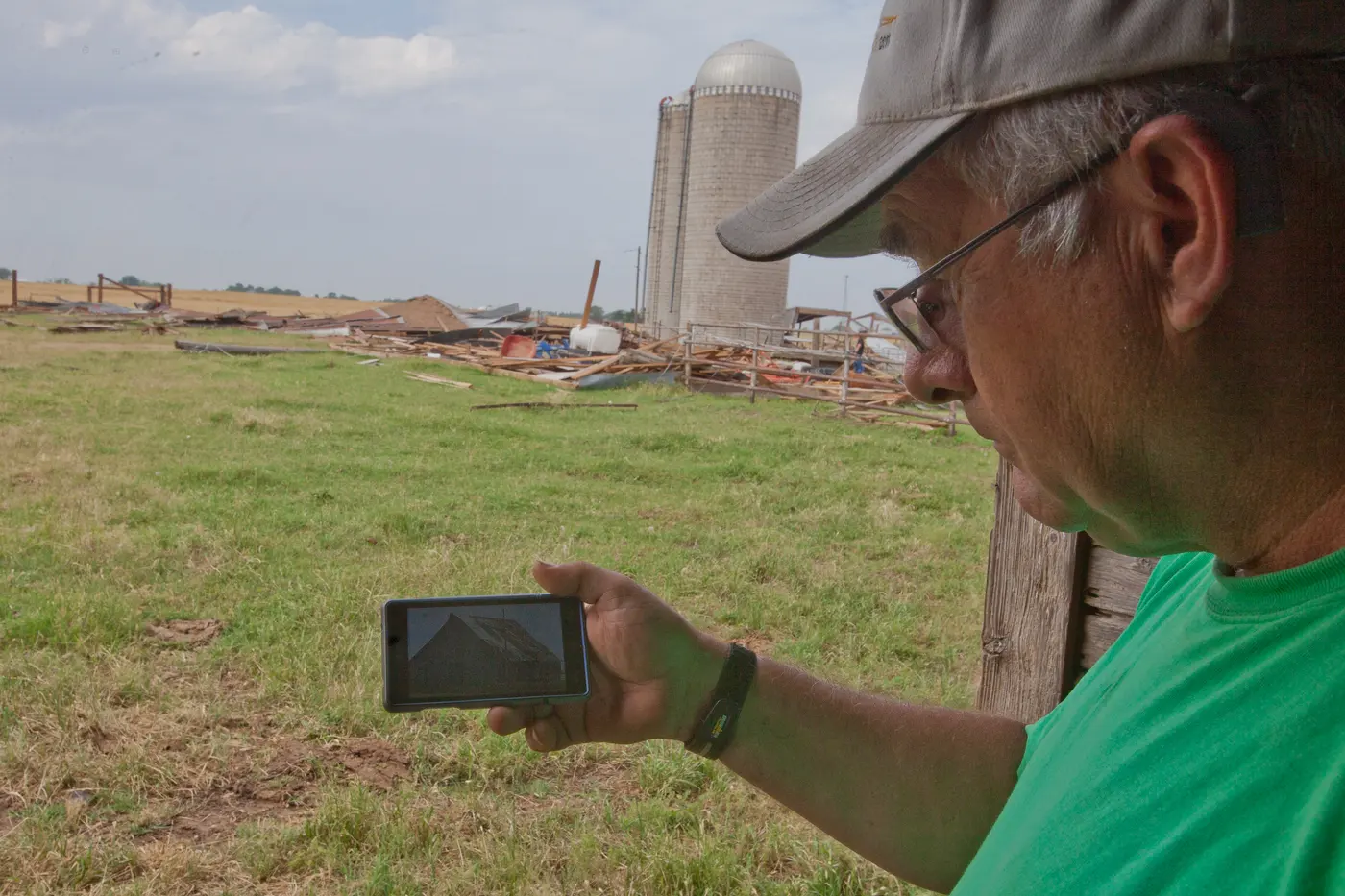 An El Reno resident stands in a debris field holding a photograph of the farmhouse that used to stand there.