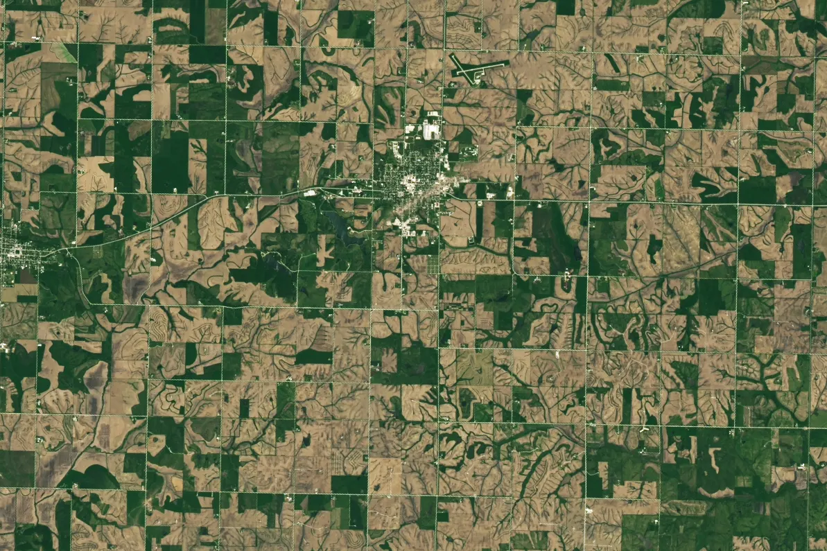 Landsat satellite view of Iowa farmland with a faint pale diagonal scar running southwest to northeast through the town of Greenfield.