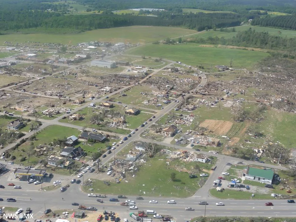 Aerial view of Hackleburg, Alabama after the tornado: block after block of foundations and debris beside a highway, with wooded hills beyond.