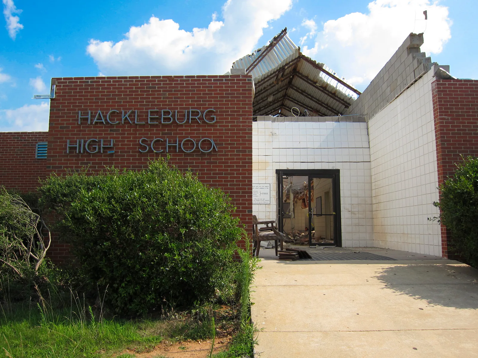 The brick entrance of Hackleburg High School with its roof torn open and ceiling panels hanging inside, photographed in July 2011.