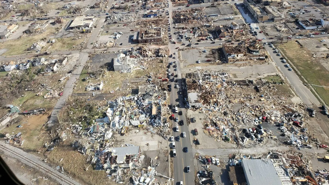 Aerial view straight down the damage swath through downtown Mayfield, with flattened brick commercial blocks either side of a cleared street.
