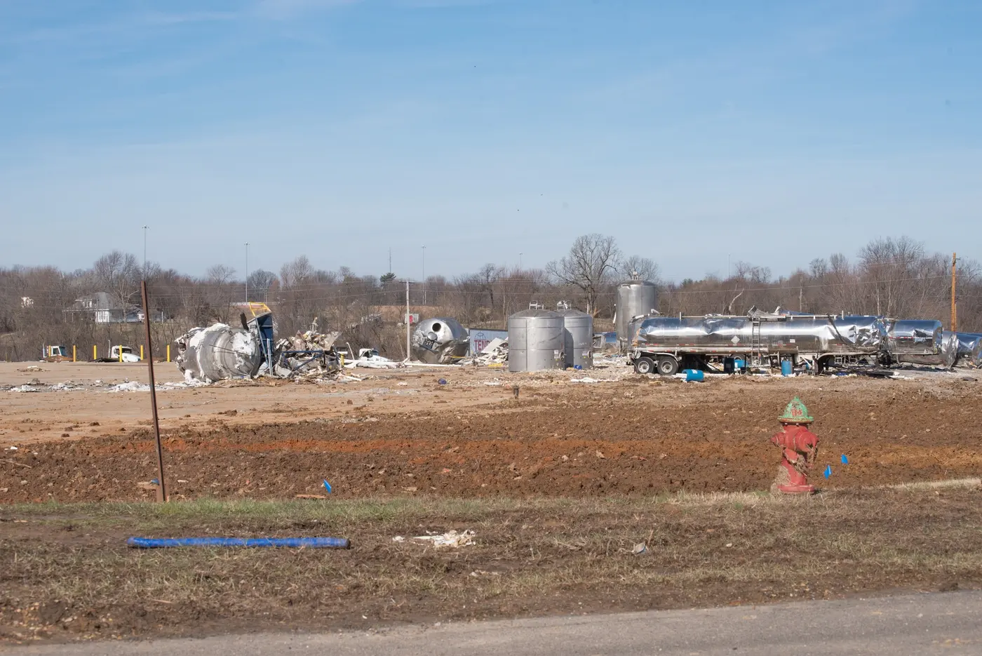 The cleared site of the Mayfield Consumer Products factory, bare graded earth with industrial vessels along the treeline.