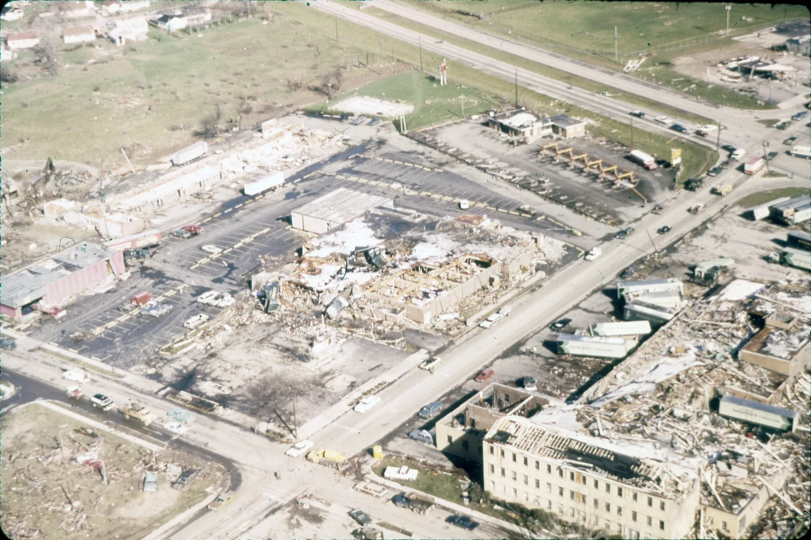 Colour aerial photograph of a destroyed shopping centre and car park in Xenia, with a stripped supermarket, a wrecked apartment building and scattered trailers.