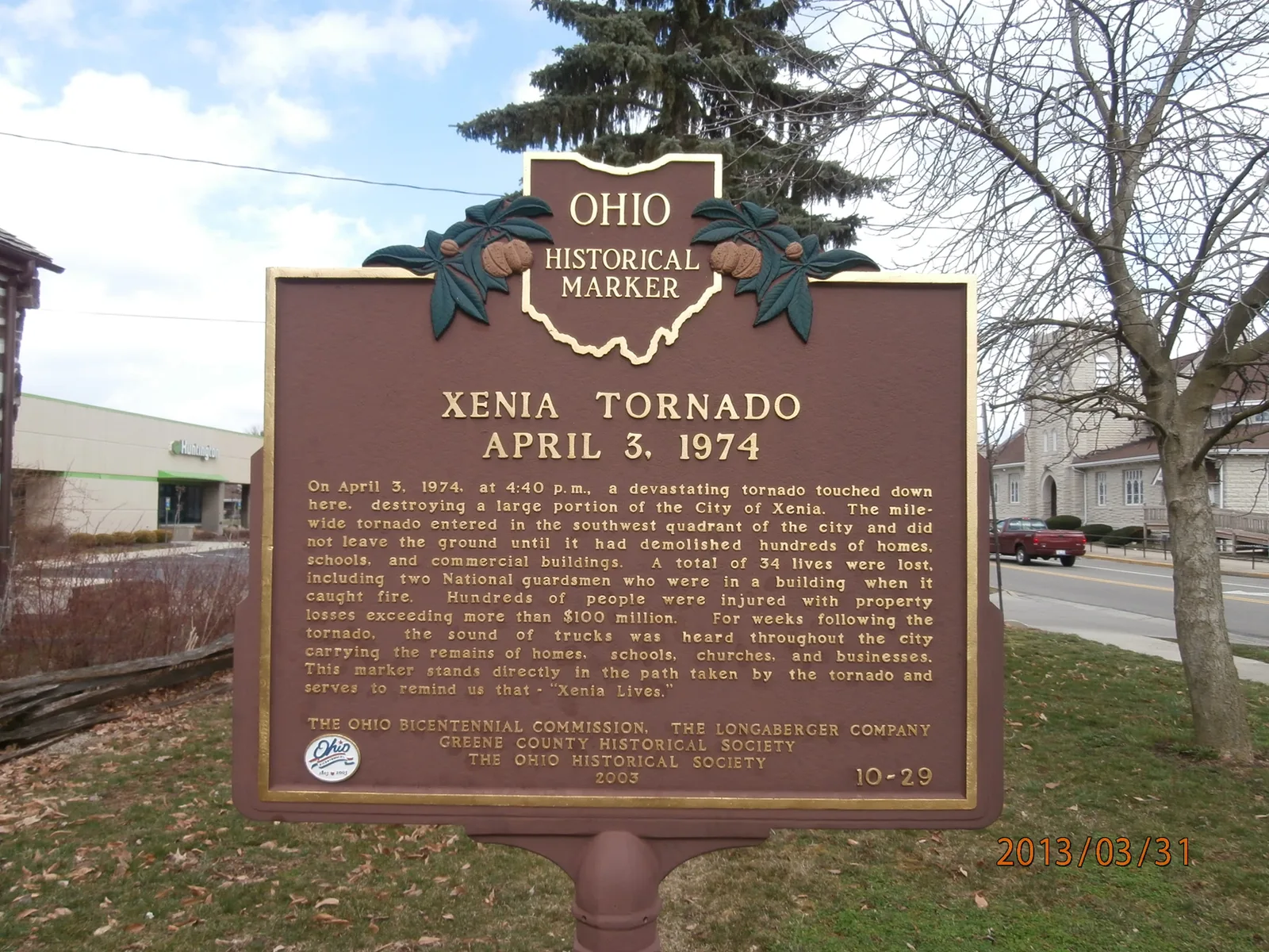 An Ohio Historical Marker headed Xenia Tornado, April 3, 1974, standing on a lawn beside a street, recording 34 lives lost and ending with the words Xenia Lives.